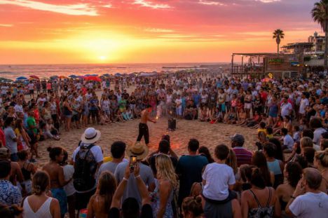 Playas llenas de familias disfrutan del verano mientras niños juegan en la arena y se observa un espectáculo callejero.