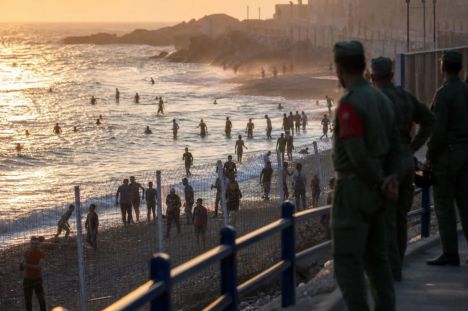 Migrantes en la frontera de Ceuta intentan cruzar mientras fuerzas marroquíes observan al atardecer.