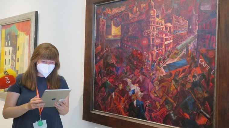 Ana Gómez leyendo un texto de George Grosz junto a su obra Metrópolis