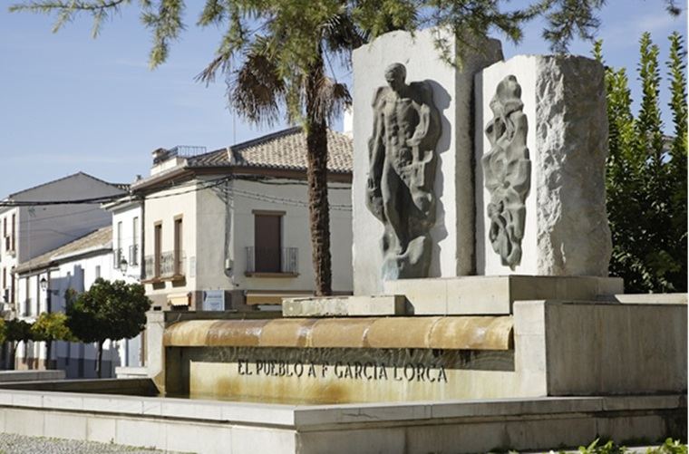 Escultura de Federico García Lorca ubicada en el Paseo del Prado de Fuente Vaqueros. Al fondo, la casa natal del poeta